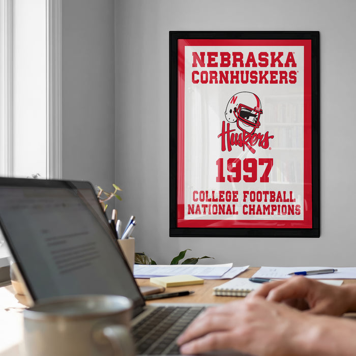 a framed poster of the Nebraska Cornhuskers from 1997, with a person's hands typing on a laptop in the foreground.