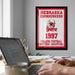a framed poster of the Nebraska Cornhuskers from 1997, with a person's hands typing on a laptop in the foreground.
