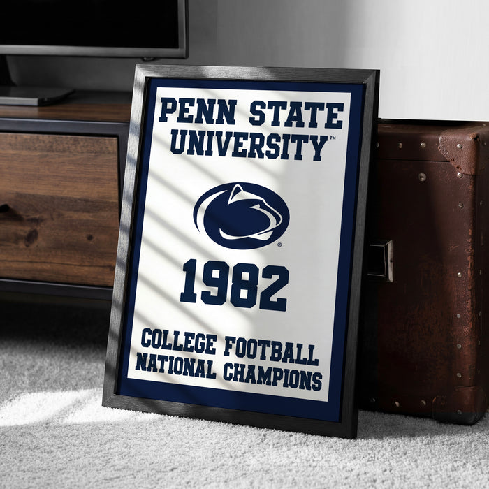 A framed poster with the text "Penn State University 1982 College Football National Champions" is displayed on a carpeted floor next to a wooden chest.