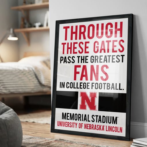 A framed poster with text that reads "THROUGH THESE GATES PASS THE GREATEST FANS IN COLLEGE FOOTBALL. N MEMORIAL STADIUM UNIVERSITY OF NEBRASKA LINCOLN"