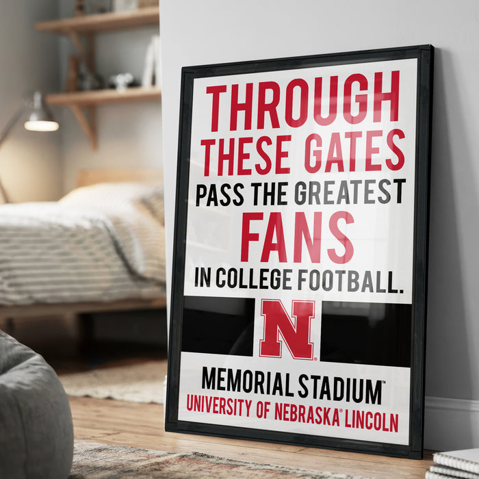 A framed poster with text that reads "THROUGH THESE GATES PASS THE GREATEST FANS IN COLLEGE FOOTBALL. N MEMORIAL STADIUM UNIVERSITY OF NEBRASKA LINCOLN"