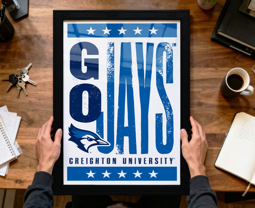 A framed poster with the text "G O JAYS" and the logo of Creighton University is being held by a person's hands.
