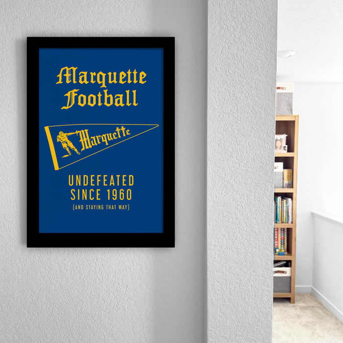 a framed poster of Marquette Football with a blue background and yellow accents, hanging on a wall.