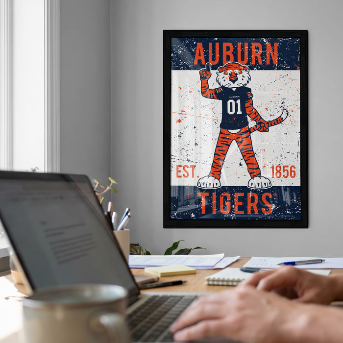 a framed poster of an animated tiger character, with the text "Auburn Tigers" displayed prominently. In the foreground, there is a laptop computer and a person's hands typing on the keyboard.