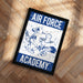 a framed poster with the text "AIR FORCE ACADEMY" and an illustration of a bird, likely representing the Air Force Academy.