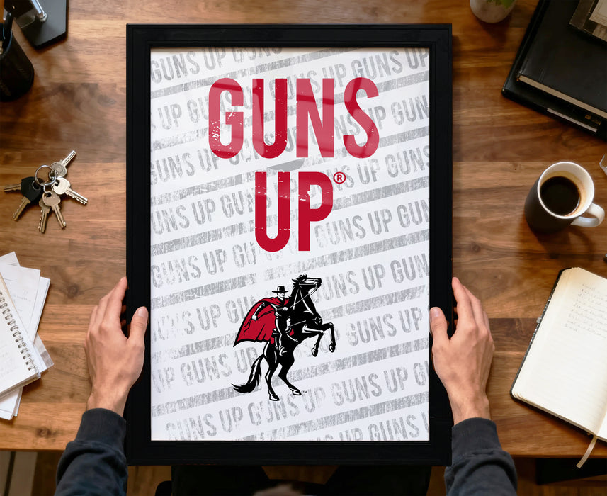 A person is holding up a framed poster with the text "GUNS UP" on it, which appears to be a promotional or informational poster related to guns.