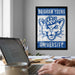 A framed poster of the University of Utah's mascot is displayed on the wall above a desk with a laptop, a coffee mug, and some papers.
