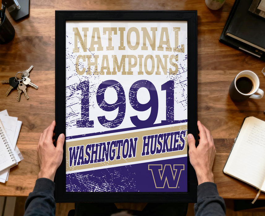 A framed poster with the text "NATIONAL CHAMPIONS 1991 WASHINGTON HUSKIES" is being held by a person's hands.