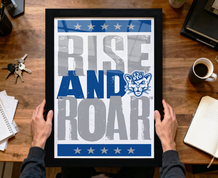 A framed poster with the text "RISE AND ROAR" and a cat logo is being held by a person's hands.