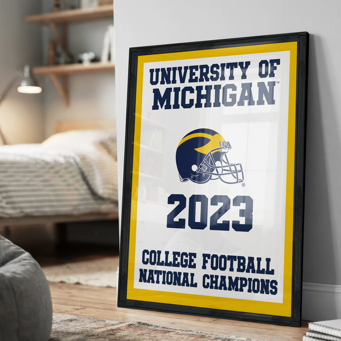 A framed poster on a wall, featuring the text "UNIVERSITY OF MICHIGAN" and "2023 COLLEGE FOOTBALL NATIONAL CHAMPIONS" along with a football helmet graphic.