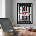 a person working on a laptop at a desk, with a framed poster featuring the text "EXIT LIGHT" in the background.