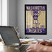 a framed poster of a mascot, a dog, with the text "WASHINGTON EST. 1861 HUSKIES" on it, hanging on a wall above a desk with a laptop and other items.