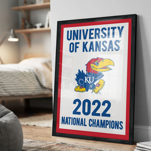 A framed poster on a wall, featuring the text "UNIVERSITY OF KANSAS" and "2022 NATIONAL CHAMPIONS" along with an illustration of a bird, likely representing the University of Kansas.