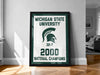A framed poster celebrating the Michigan State University's 32-7 National Champions, with the text "MICHIGAN STATE UNIVERSITY" and "2000 NATIONAL CHAMPIONS" prominently displayed.
