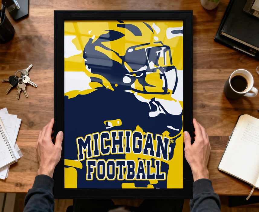 A framed poster of a football player in a yellow uniform is being held by a person's hands, with a desk and various items in the background.