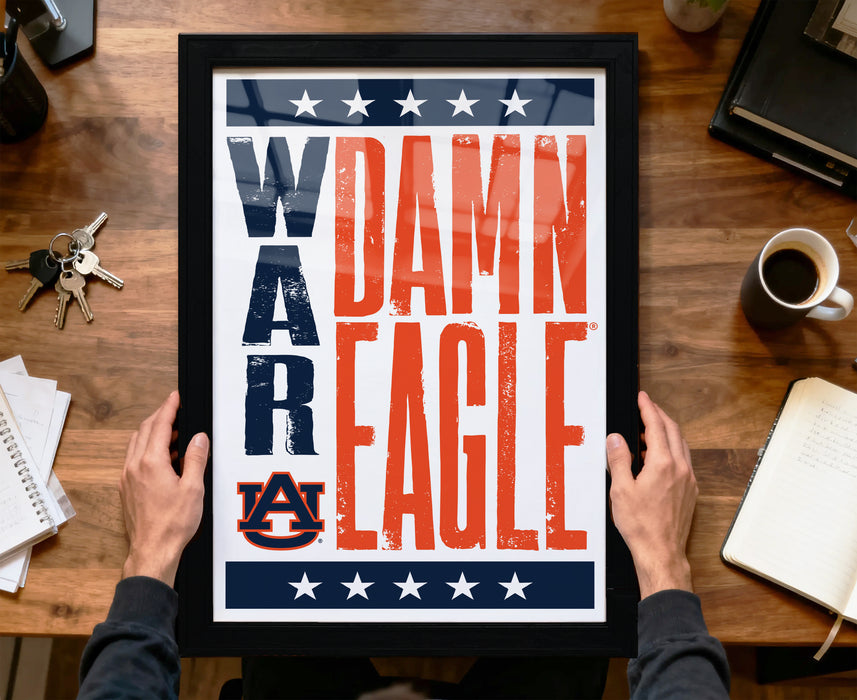 A framed poster with the text "DAMN EAGLE" is being held by a person's hands, with a wooden desk and various items in the background.