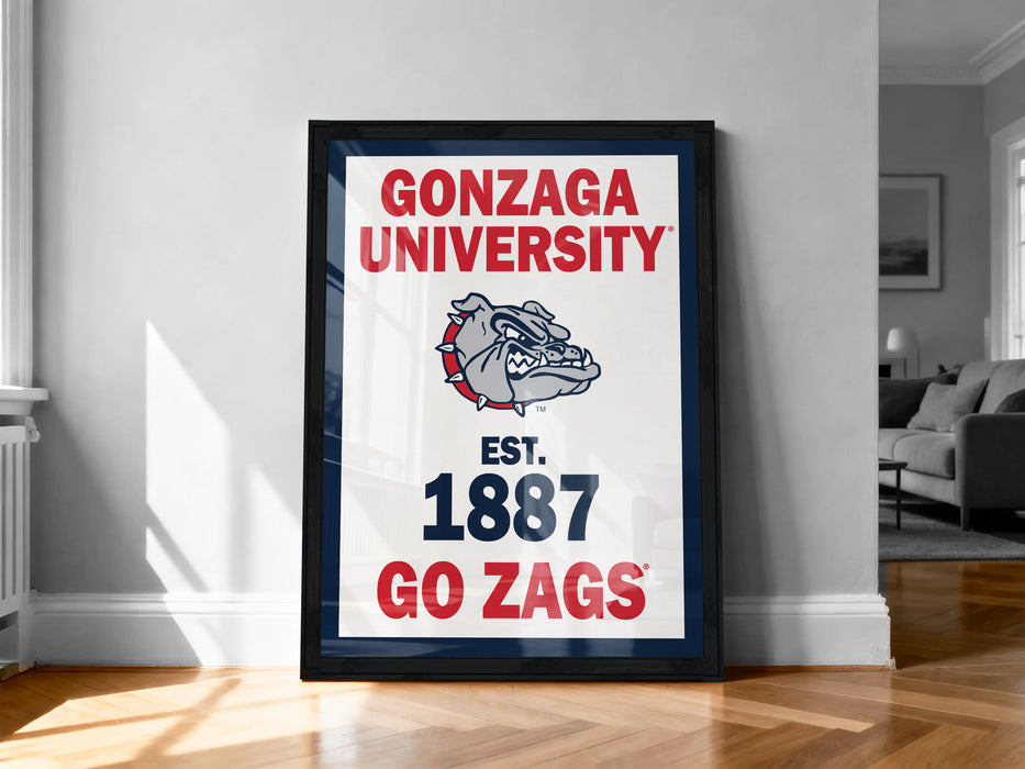 A framed poster with the text "GONZAGA UNIVERSITY EST. 1887 GO ZAGS" and a bulldog logo, standing on a wooden floor against a white wall.