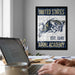 a framed poster of a naval emblem hanging on a wall, with a laptop and a person's hands visible in the foreground.