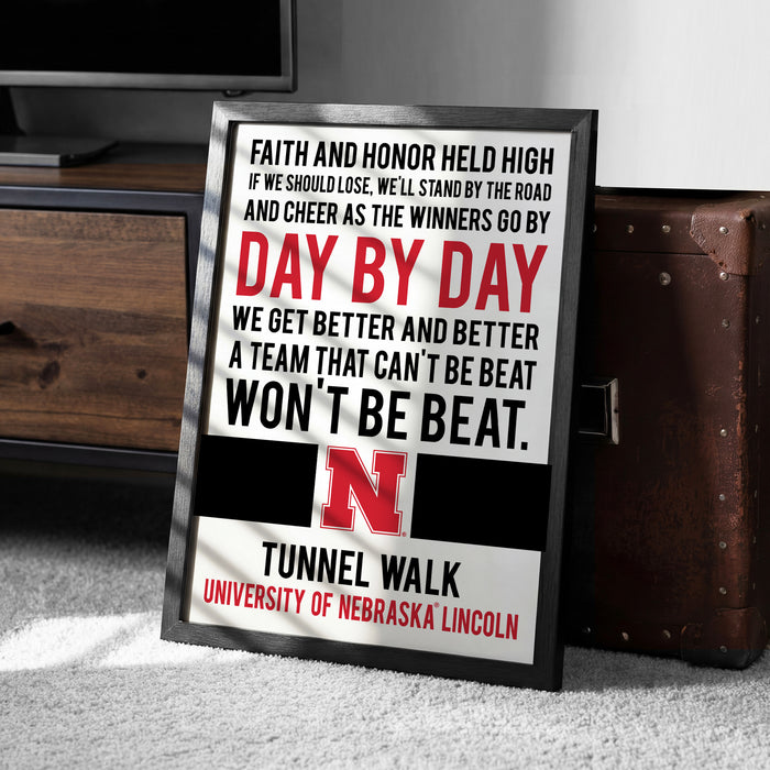 a framed motivational poster with a quote about Nebraska football, placed on a carpeted floor next to a wooden chest.