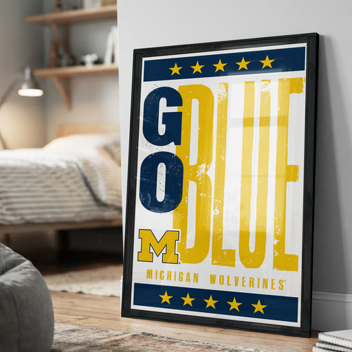 A framed poster with the text "GO BLUE MICHIGAN WOLVERINES" displayed prominently on it, along with a border of yellow stars.