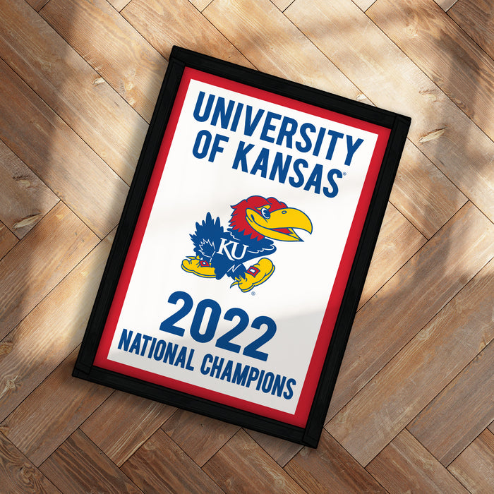 A framed poster with the text "UNIVERSITY OF KANSAS" and a graphic of a bird, likely representing the University of Kansas. The poster also includes the text "2022 NATIONAL CHAMPIONS" and features a red, white, and blue color scheme.