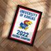 A framed poster with the text "UNIVERSITY OF KANSAS" and a graphic of a bird, likely representing the University of Kansas. The poster also includes the text "2022 NATIONAL CHAMPIONS" and features a red, white, and blue color scheme.
