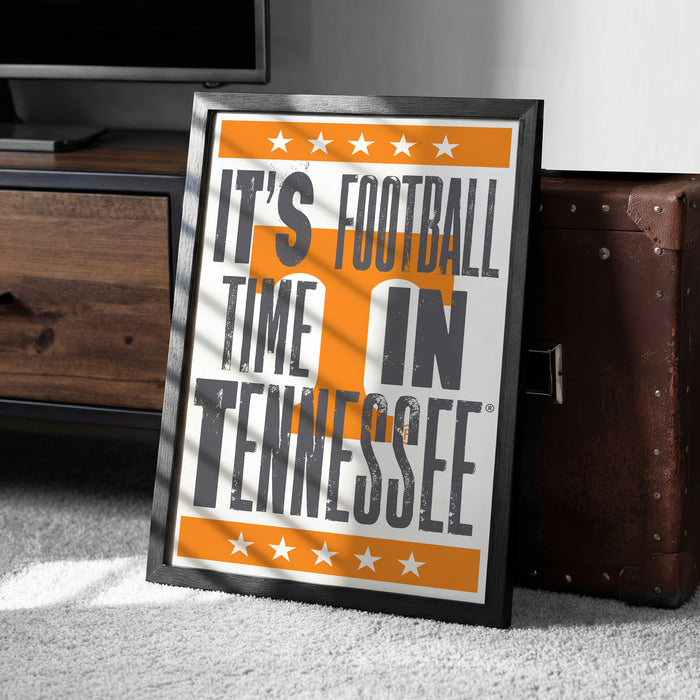 A framed poster with the text "IT'S FOOTBALL TIME IN TENNESSEE" is displayed on a carpeted floor next to a wooden chest.