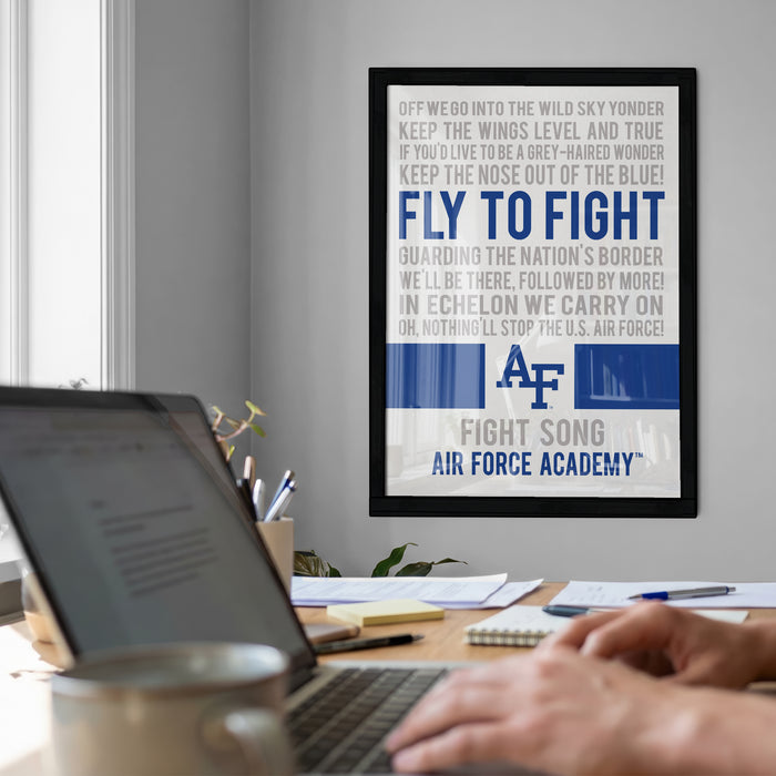 a framed poster with a motivational message about the Air Force, displayed on a wall above a desk with a laptop and other items.