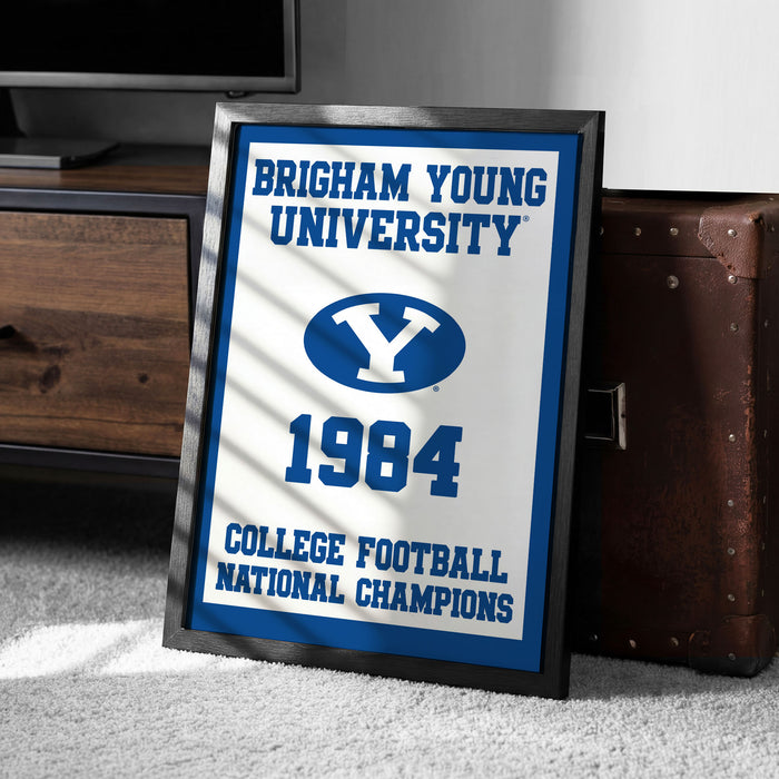 A framed sign displaying the text "BRIGHTAM YOUNG UNIVERSITY" and "COLLEGE FOOTBALL NATIONAL CHAMPIONS" along with a blue and white logo, indicating a celebration of the university's college football national championship victory in 1984.