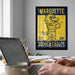 a framed poster of a cartoon eagle on a wall, with a laptop and a coffee cup on a desk in the foreground.