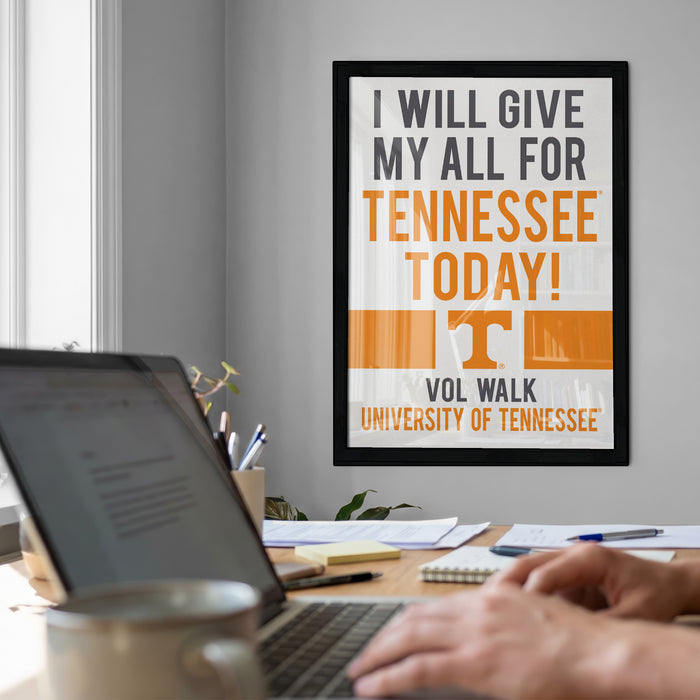 a framed poster with the text "I WILL GIVE MY ALL FOR TENNESSEE TODAY!" and "VOL WALK UNIVERSITY OF TENNESSEE" on a wall, with a person's hands typing on a laptop in the foreground.