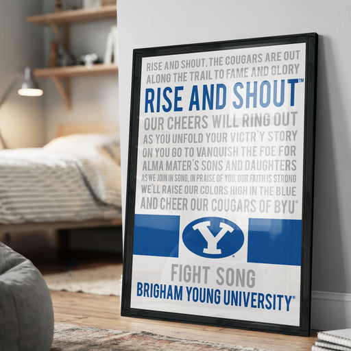 a framed poster with text and a logo, located in a room with a bed and a bookshelf in the background.