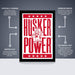 The image is a poster featuring the word "HUSKER" in large red letters, with a smaller "POWER" below it. The poster is described as " Officially licensed" and "Premium printed", indicating that it is a high-quality, professionally printed poster. The poster is also referred to as a "Shipped flat" and "The perfect gift", suggesting that it is a thoughtful and attractive gift option.