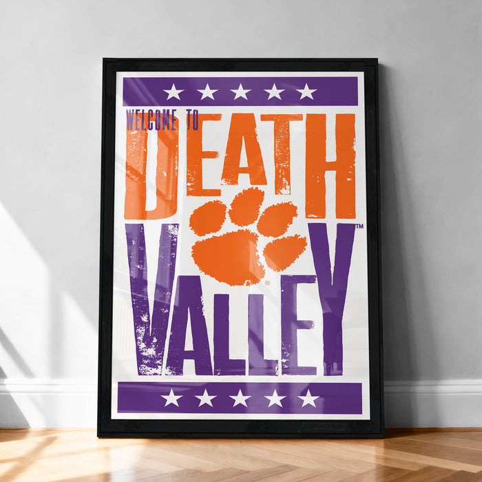 A framed poster with the text "Welcome to Death Valley" and an orange paw print, placed on a wooden floor against a white wall.