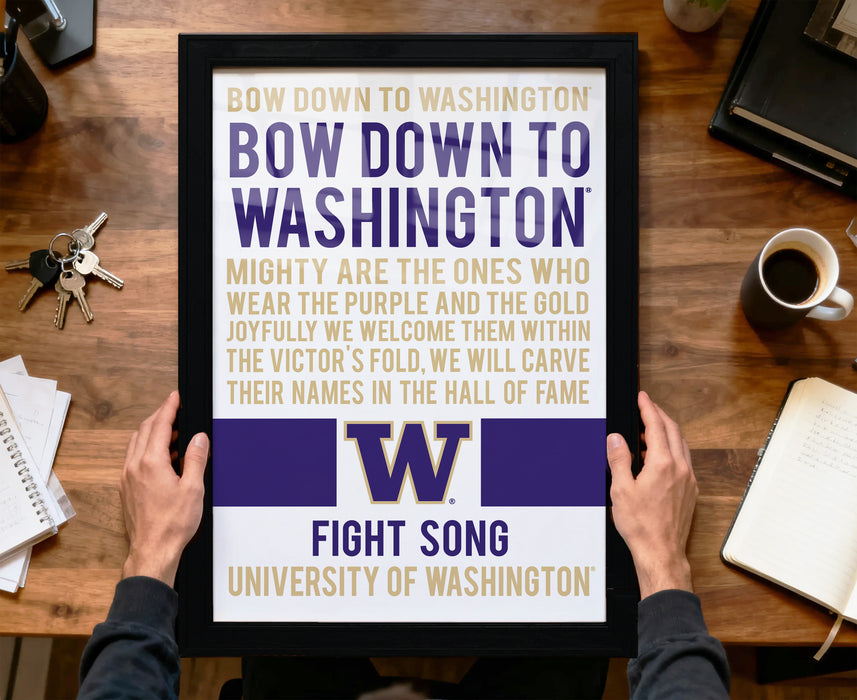 A framed poster with text is being held by a person's hands, placed on a wooden desk.