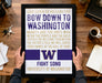 A framed poster with text is being held by a person's hands, placed on a wooden desk.