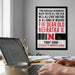 a framed poster with a quote about Nebraska, a laptop on a desk, and a person's hands typing on the keyboard.