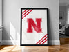 A framed poster with a large red letter "N" on a white background, placed on a wooden floor against a white wall.