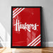 A framed poster with the word "Huskies" written in white cursive text against a red background.