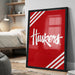 A framed poster with the word "Huskies" written on it, displayed on a wall in a bedroom setting.