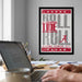 a framed poster with the text "ROLL TIDE ROL" and "ALABAMA GRIMON TIDE" on it, hanging on a wall above a desk with a laptop and other items on it.