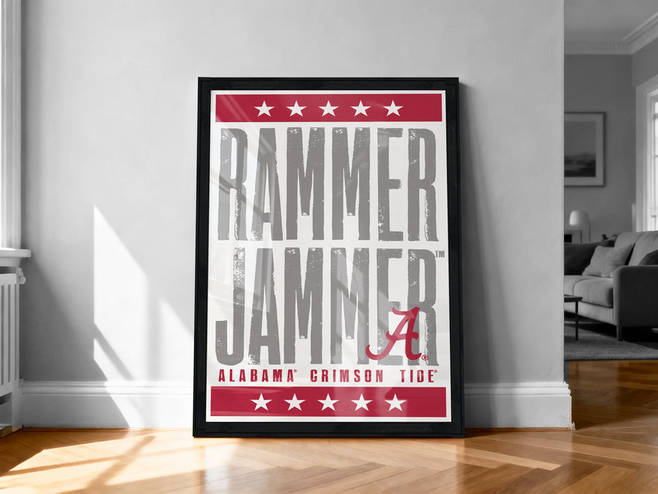 a framed poster with the text "RAMMER JAMMER" and "ALABAMA CRIMSON TIDE" on it, standing on a wooden floor against a white wall.