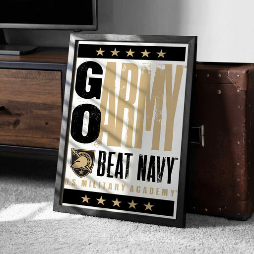 A framed poster with the text "GO ARMY BEAT NAVY" and a military insignia, placed on a carpeted floor next to a wooden chest.