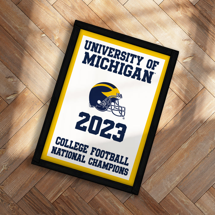A framed poster with the text "UNIVERSITY OF MICHIGAN" and "2023" on it, along with a football helmet and the text "COLLEGE FOOTBALL NATIONAL CHAMPIONS".