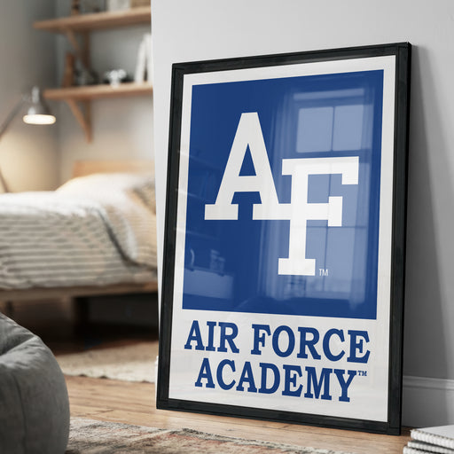 a framed poster with the Air Force Academy logo, placed on a wall in a bedroom setting.