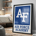 a framed poster with the Air Force Academy logo, placed on a wall in a bedroom setting.