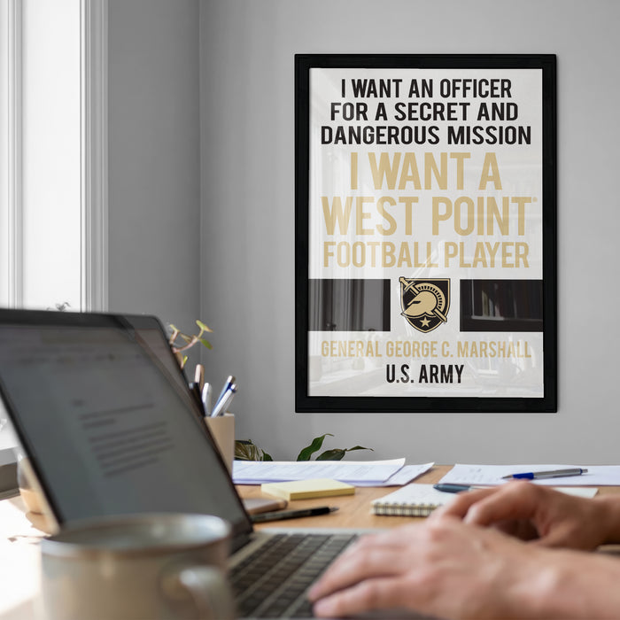 a framed poster with a quote about wanting an officer for a secret and dangerous mission, along with a football player's logo. In the foreground, there is a laptop and a coffee cup on a desk, suggesting a workspace or home office setting.