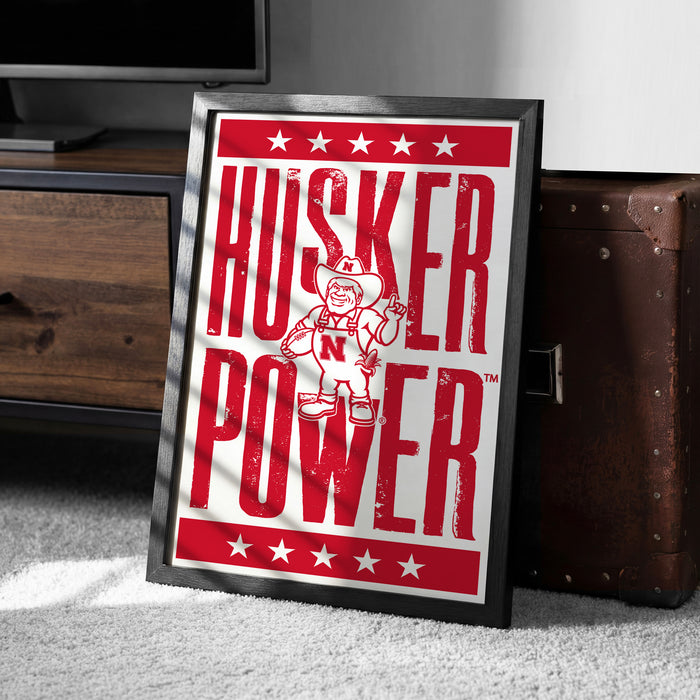 A framed poster with the text "HUSKER POWER" and a graphic of a person wearing a hat and holding a football.