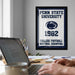 A framed poster of Penn State University from 1982 hangs on a wall, with a laptop and a coffee mug on a desk in the foreground.