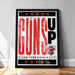 A framed poster with the text "GUNS UP" prominently displayed, along with a graphic of a character wearing a gun. The poster is set against a white wall and has a black border.